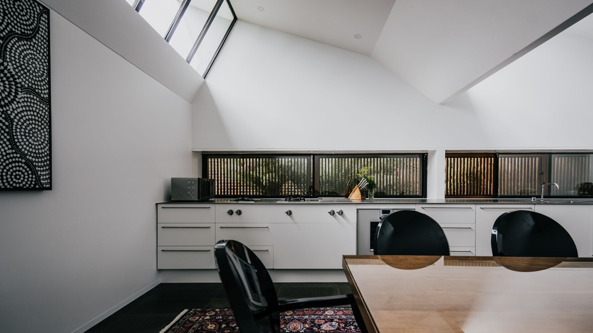 A modern kitchen with a skylight, white cabinets, and a dining area with a wooden table and chairs.