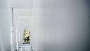 Un pasillo estrecho y blanco con una puerta al final que da a una habitación con una mesa y una silla.