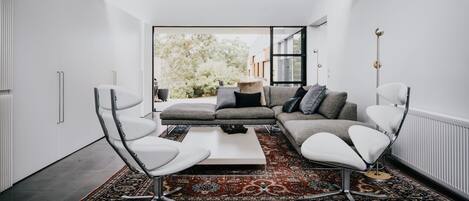 Una sala de estar moderna con un sofá gris, sillones blancos, una mesa de centro y un tapete estampado.