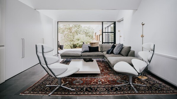 A modern living room with a grey sofa, white armchairs, a coffee table, and a patterned rug. - Alkina Lodge Yani is the ultimate base for your Great Ocean Road adventure. (Wattle Hill)