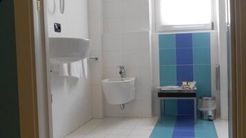Un baño con un lavamanos blanco, un lavabo pedestal pequeño, una ventana y una pared con azulejos azules.