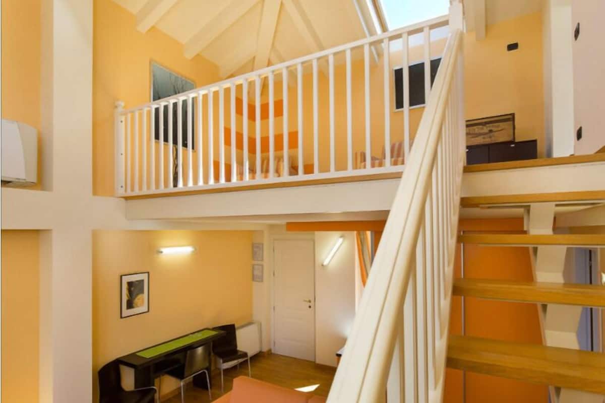A multi-level room with a balcony, a desk with chairs, and a couch.