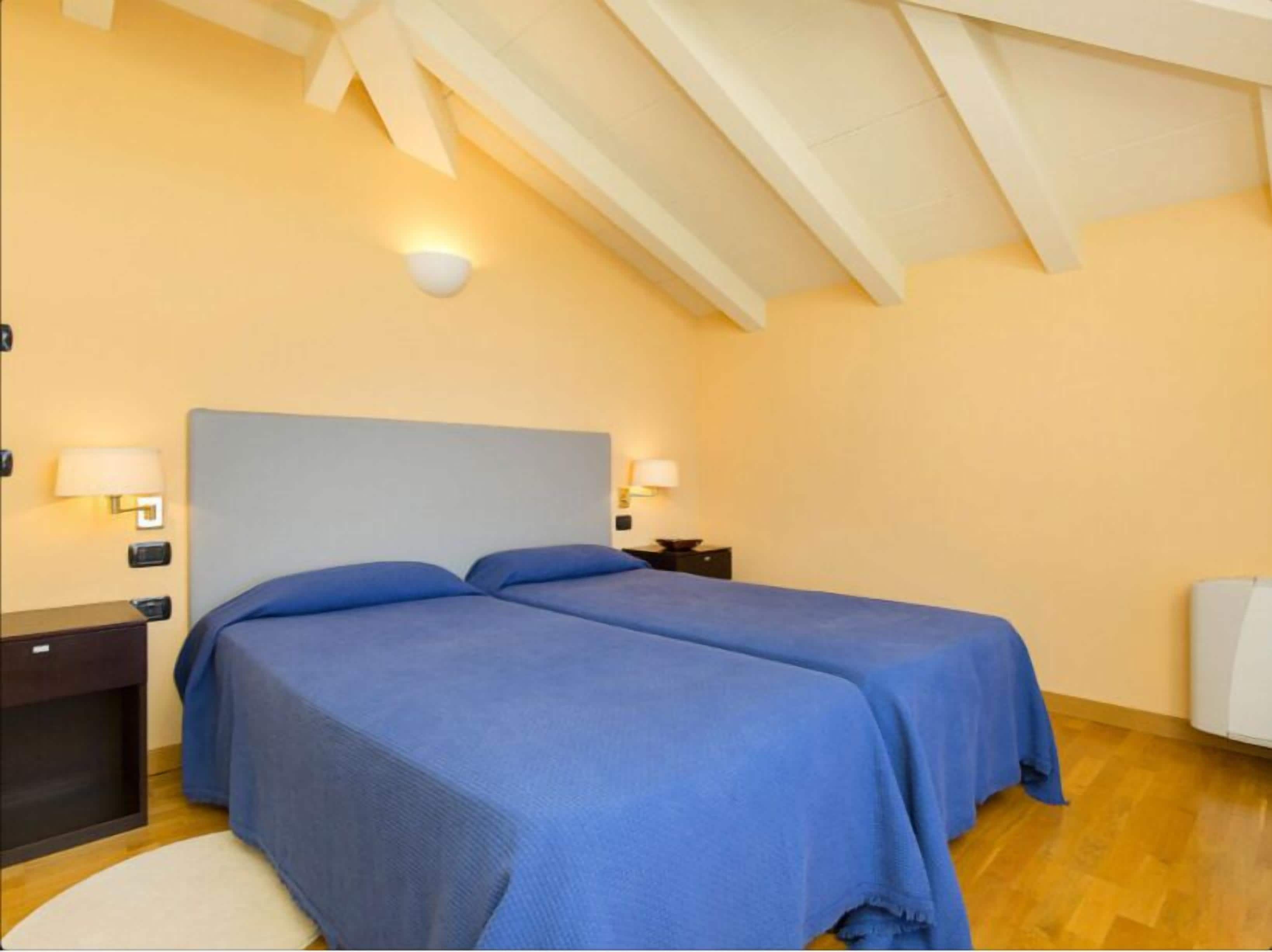 A bedroom with two beds, wooden flooring, and a sloped ceiling with exposed beams.