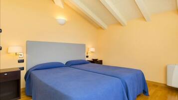 A bedroom with two beds, wooden flooring, and a sloped ceiling with exposed beams.