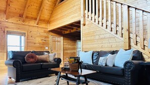 A log cabin interior with two leather sofas, a coffee table, and a wooden staircase.