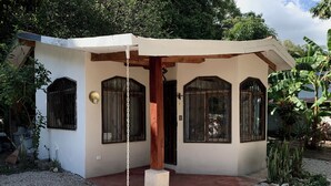 A small, single-story building with a porch, a concrete base, and a gravel driveway.