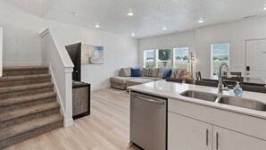 Een moderne keuken met een vaatwasser, een eethoek met een tafel en stoelen, een bank met kussens, en een trap naar een ander niveau.