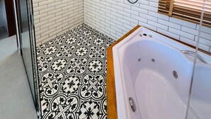 A modern bathroom with white brick walls, a black and white patterned floor, a wooden-framed bathtub, and a glass shower enclosure. - Luxury loft with jacuzzi, Casinhas do morro. (Gamboa)