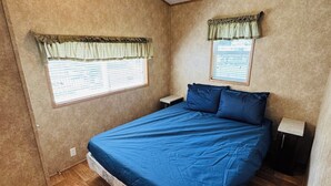 Een slaapkamer met een groot bed, twee ramen met gordijnen, een plafondventilator en houten vloeren.