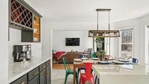Een moderne keuken met een centraal eiland, een ingebouwde wijnkast en een eethoek met kleurrijke stoelen.