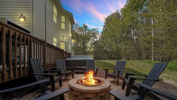Een vuurkuil omringd door stoelen, een barbecue en een huis met een terras.