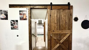 A hallway with a wooden door leading to a bedroom. There are three framed pictures on the wall.