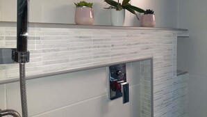 Een badkamer met een douche, een spiegel en een plank met drie plantenpotten.