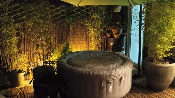 Een ronde zithoek met een overkapping, omringd door bamboe en potplanten.