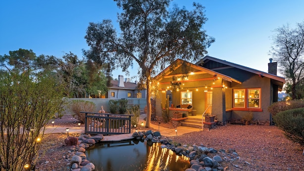 Ein Haus mit Teich, umgeben von Steinen und Bäumen, und eine Terrasse mit Lichterketten.