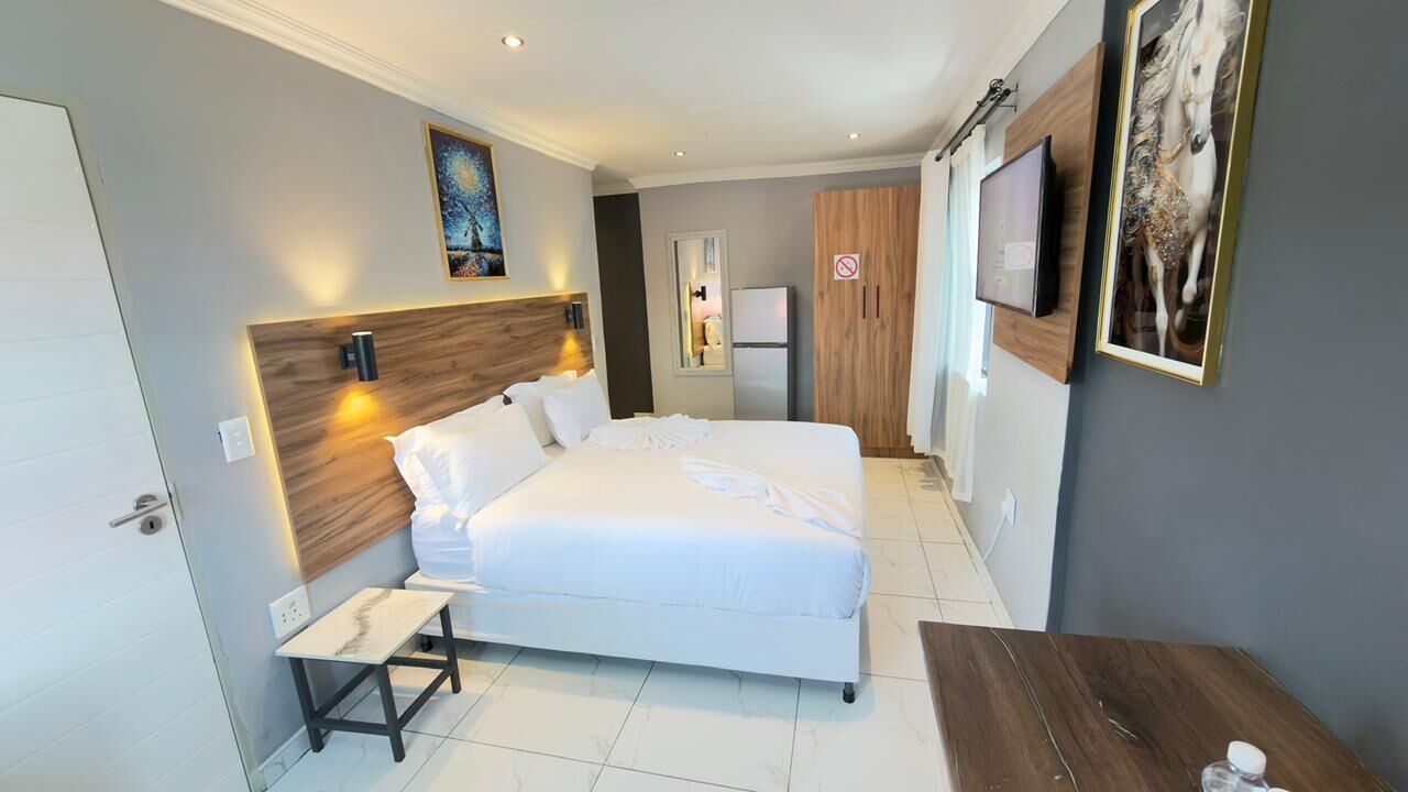 A modern hotel room with a large bed, bedside tables, a small desk, a TV, and artwork on the walls.