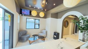 Un intérieur moderne avec un comptoir d’accueil en marbre, deux canapés, un téléviseur et une grande plante en pot.