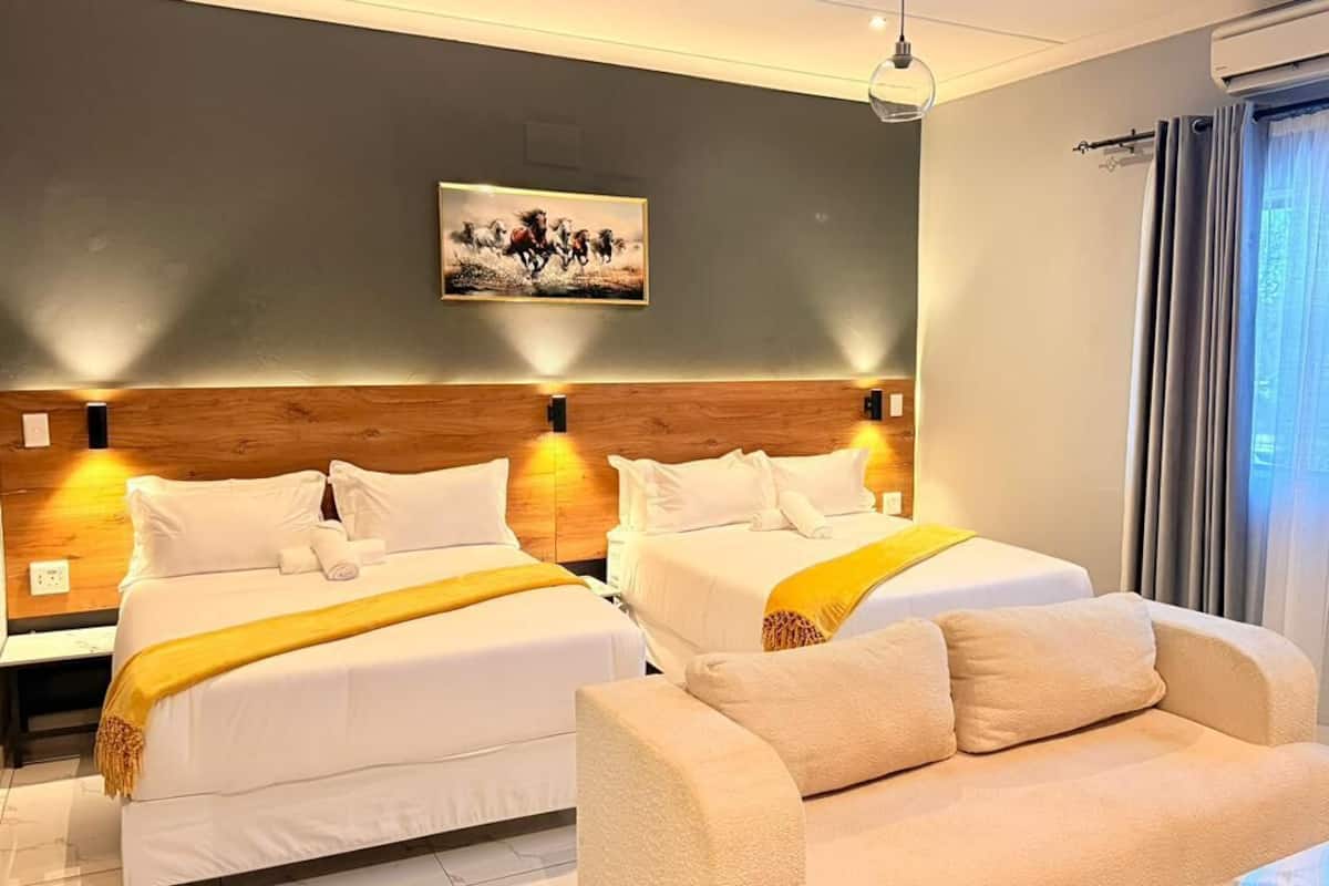 Una habitación de hotel con dos camas, un sofá, un cuadro en la pared y un ventanal con cortinas.