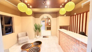 Uma área de recepção com balcão de mármore, mesa de atendimento, espaço de espera com sofá e um vaso de planta.