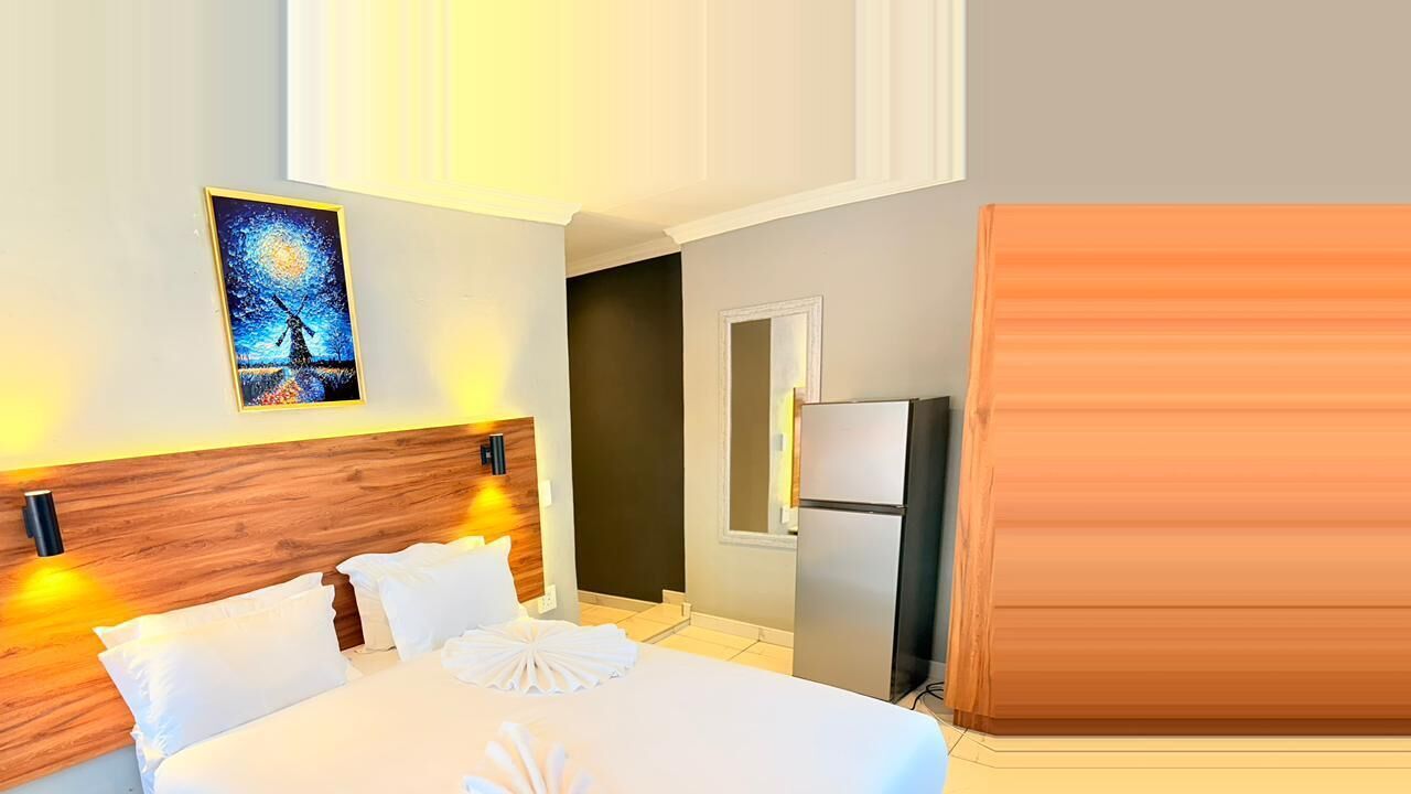 Ein Hotelzimmer mit Bett, einem Gemälde, einem Kühlschrank und einem hölzernen Kopfteil.