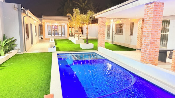 Uma área de piscina moderna ao ar livre, com uma piscina retangular, rodeada por um gramado bem cuidado e um edifício de tijolos.