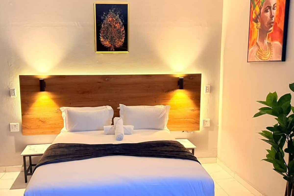 Habitación de hotel con cabecera de madera, cama con ropa de cama blanca, mesita de noche y lámpara fijada a la pared.
