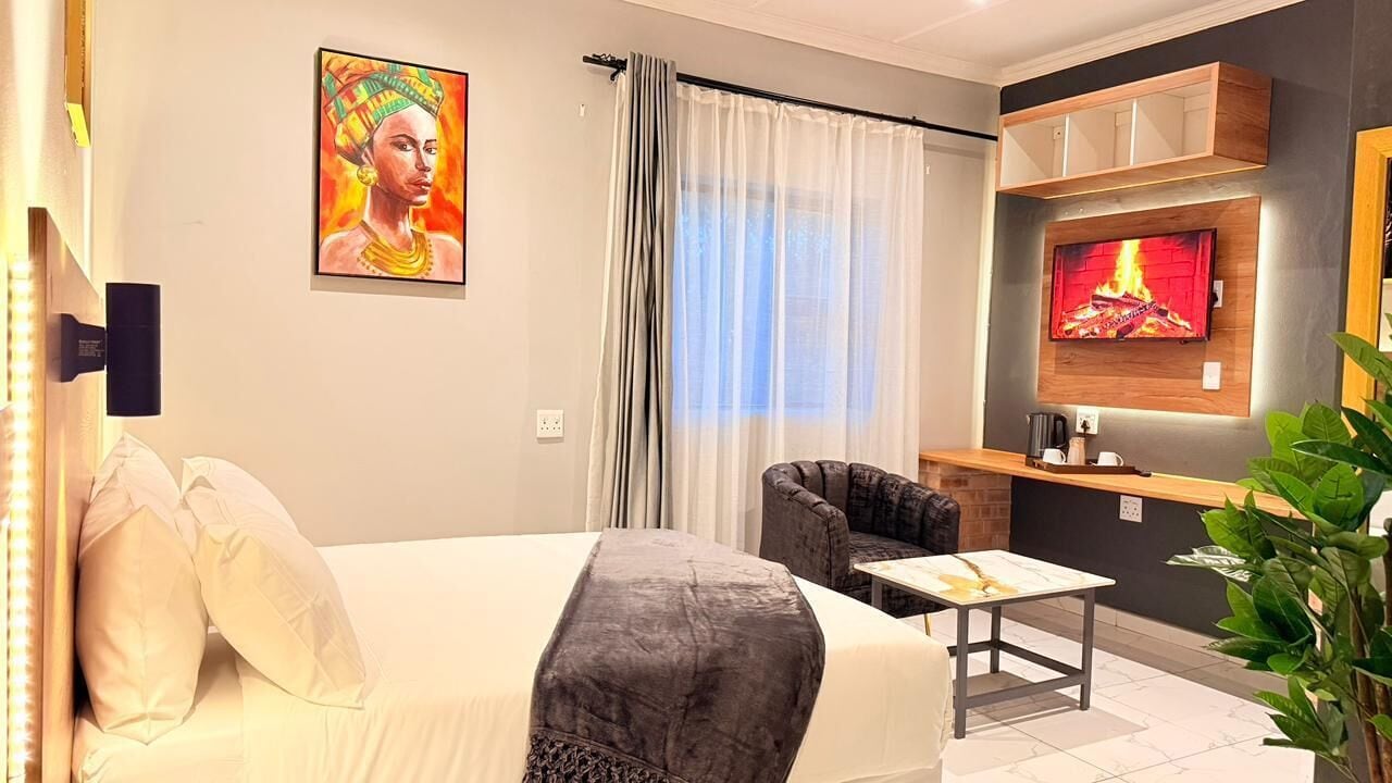 A hotel room with a bed, a sofa, a TV, a small table, and a plant.