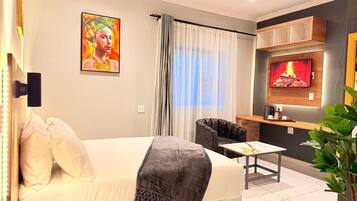 A hotel room with a bed, a sofa, a TV, a small table, and a plant.