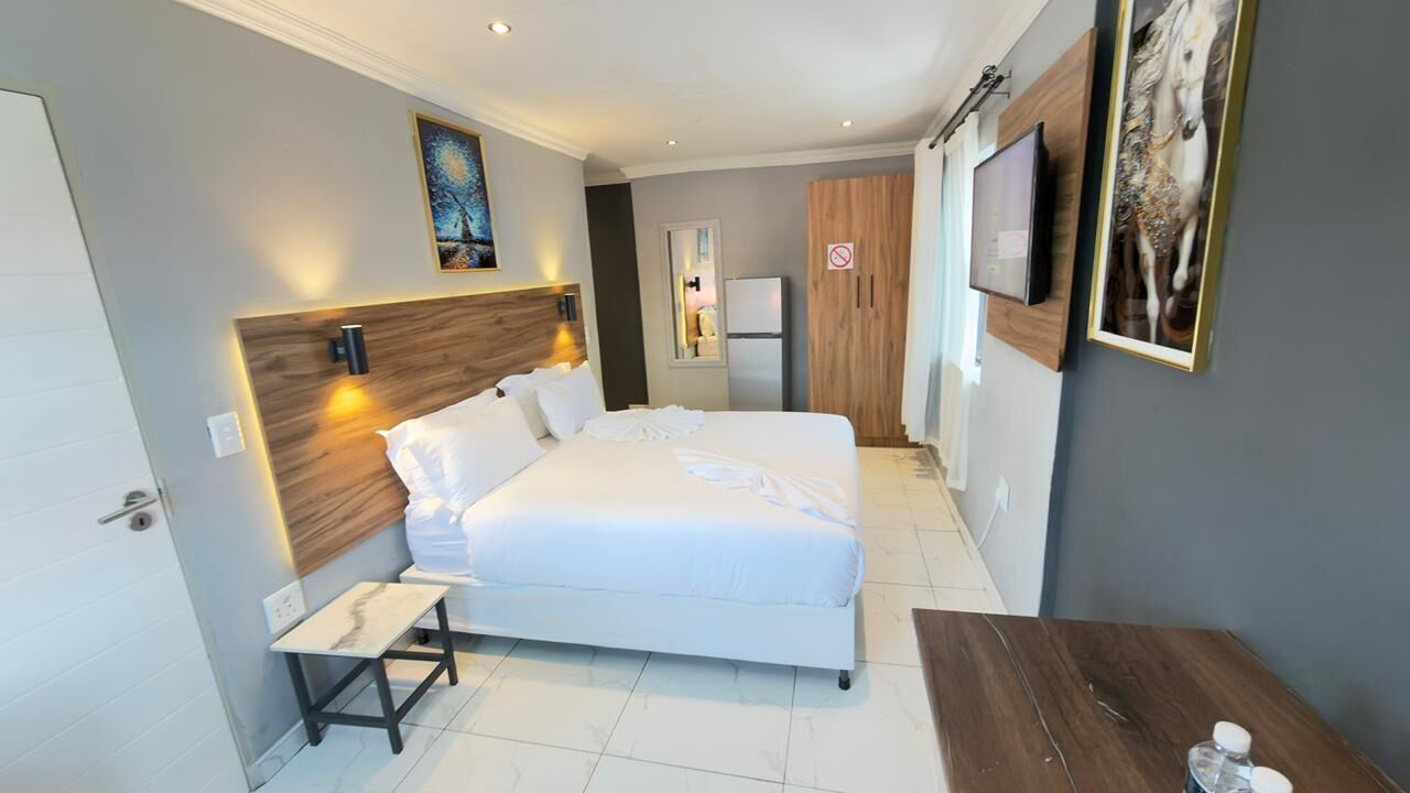 Une chambre d’hôtel moderne avec un grand lit, des tables de chevet, un bureau, une télévision et des œuvres d’art accrochées aux murs.