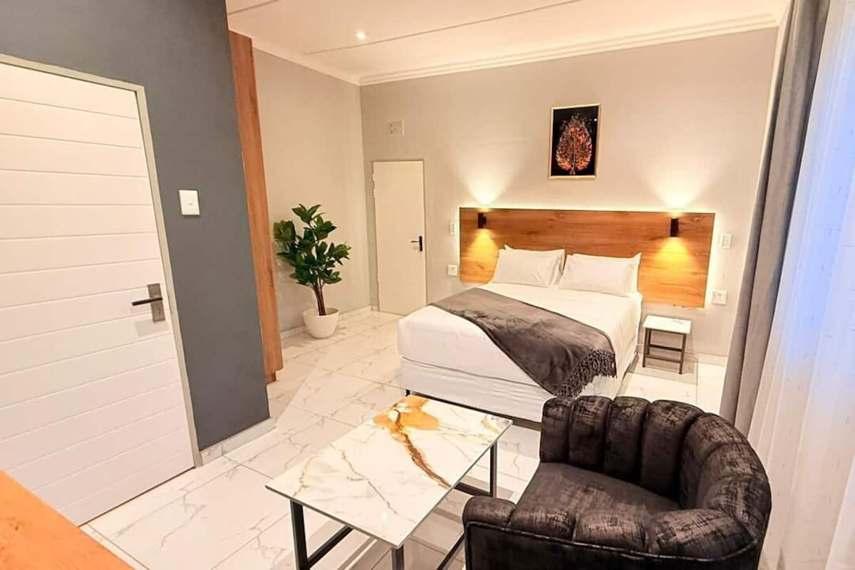Una habitación de hotel moderna con una cama, mesitas de noche, una silla, una planta en maceta y un suelo de baldosas de mármol.