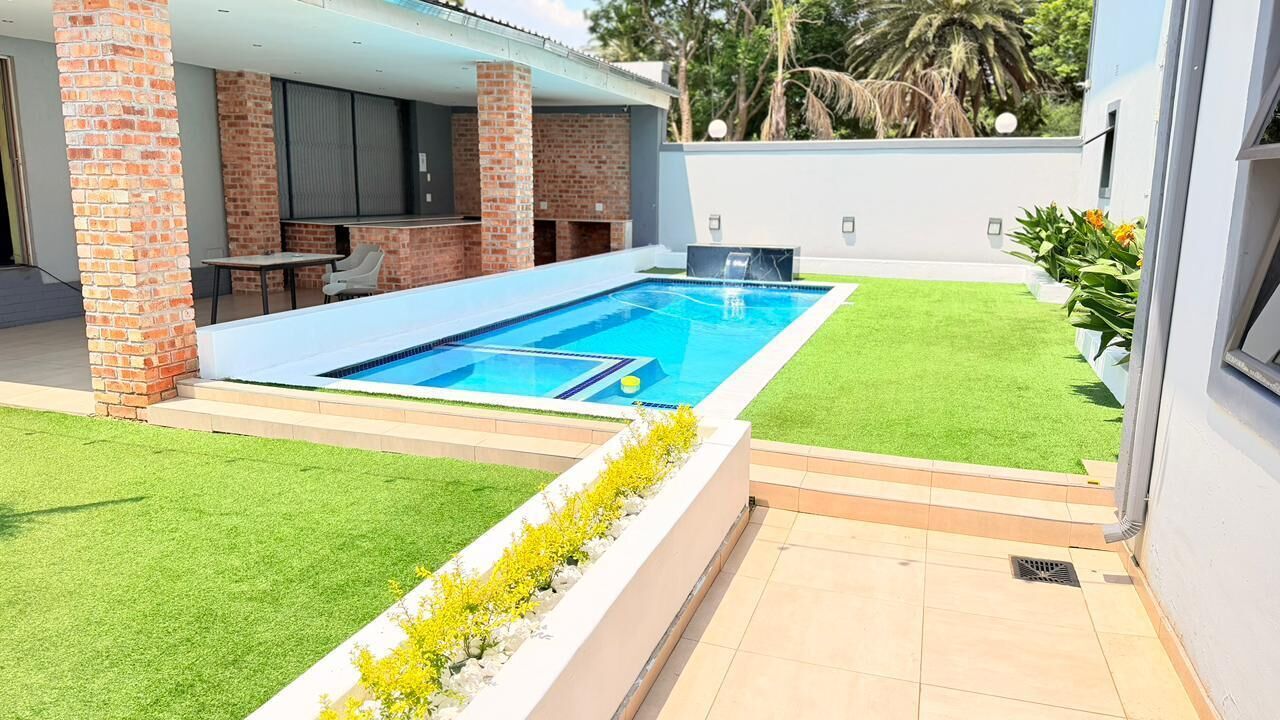 A swimming pool with a patio area, a brick column, and a grassy lawn.