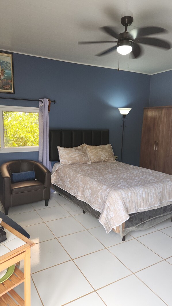 A bedroom with a bed, a chair, a desk, a ceiling fan, and a window with curtains.