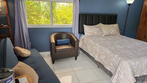 Un dormitorio con cama, una silla, un sofá y una ventana con cortinas.