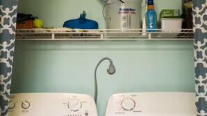 Un cuarto de lavandería con dos lavadoras de carga frontal y un estante superior con productos de limpieza.