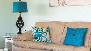 Una sala de estar con un sofá color beige, una almohada azul, una lámpara decorativa y una obra de arte en la pared.