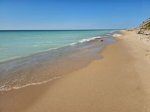 A beach with clear turquoise water, a sandy shore, and a rocky outcrop on the right.