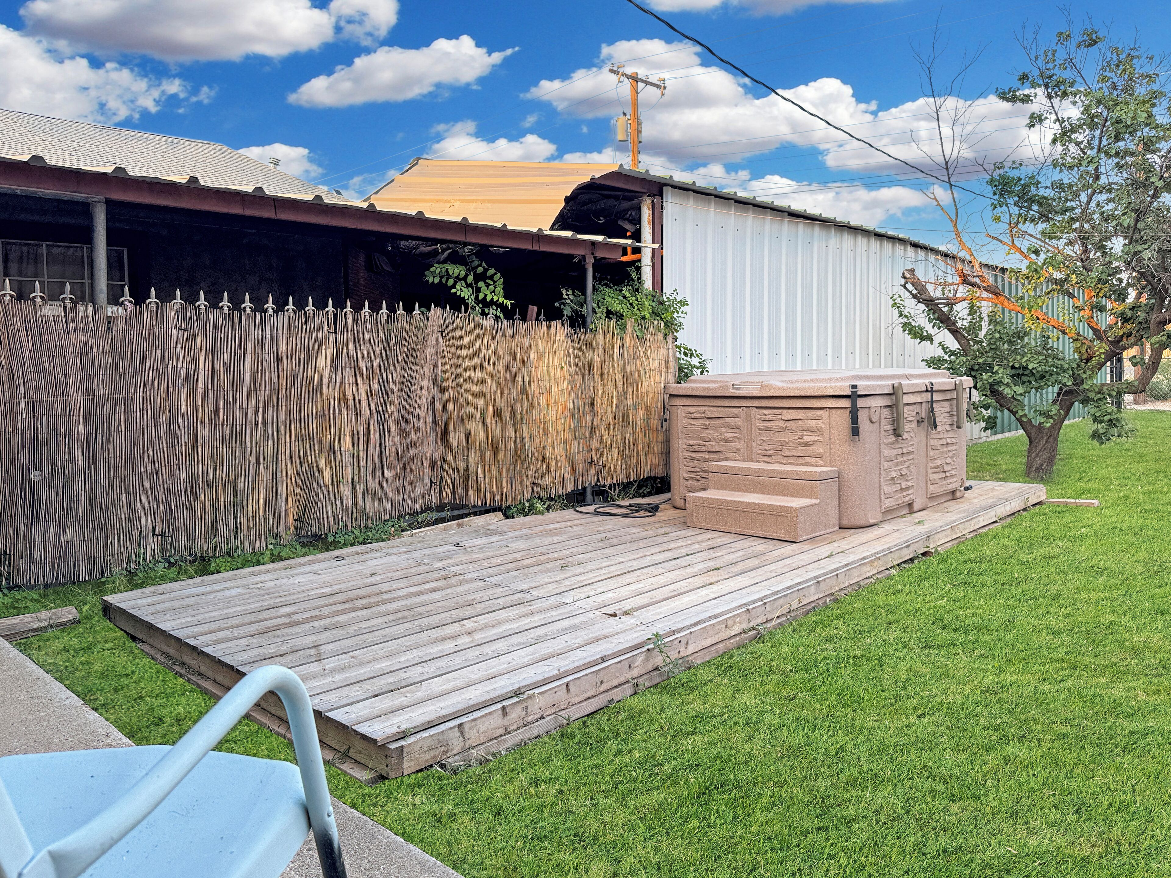 A backyard with a hot tub, wooden deck, and a fence.