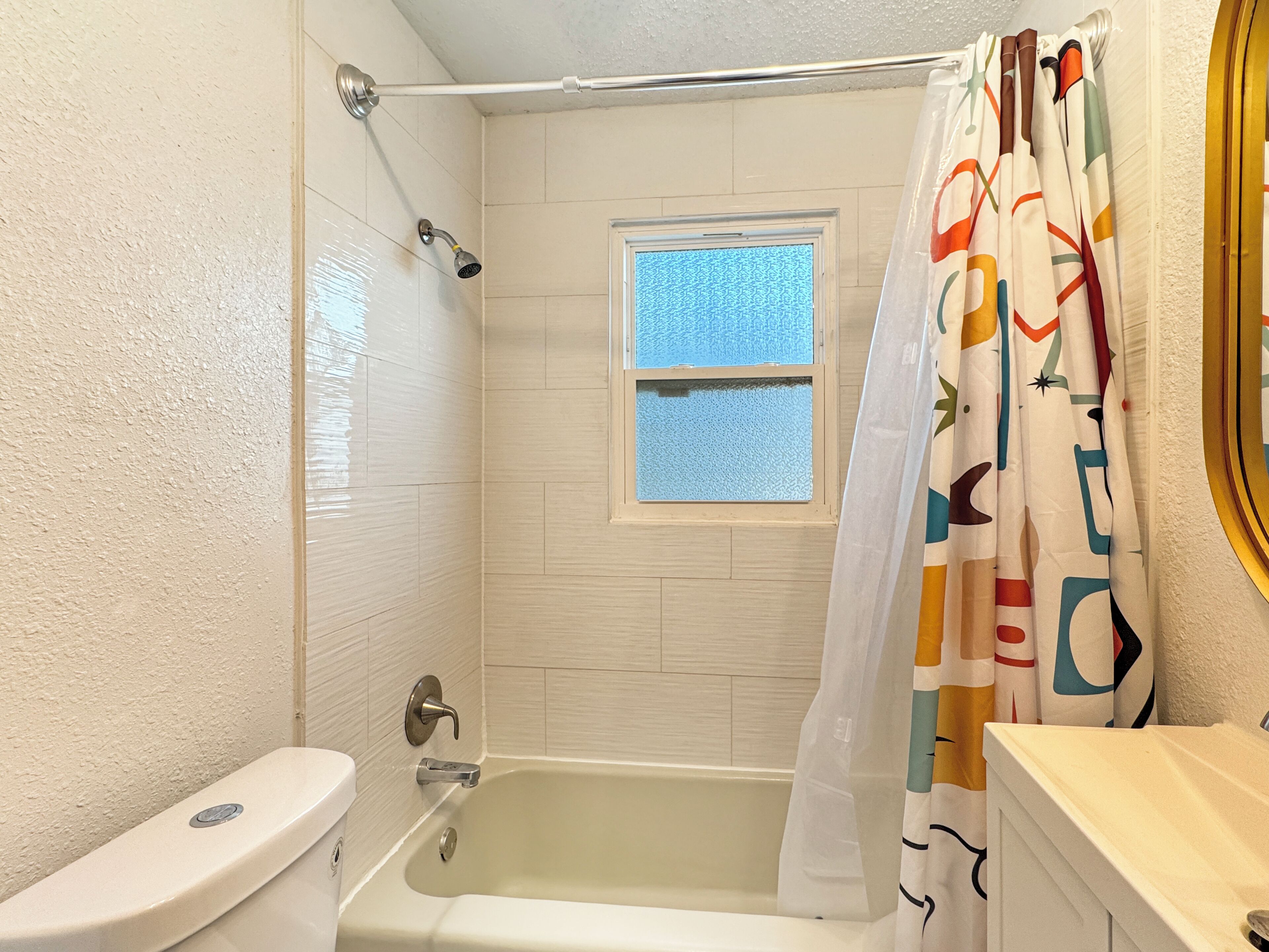 A bathroom with a bathtub, toilet, and a window.