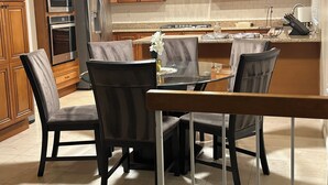 A modern kitchen with wooden cabinets, stainless steel appliances, and a glass dining table with chairs.