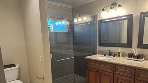 A bathroom with a glass-enclosed shower, a toilet, and a vanity with a sink and mirror.