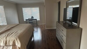 A bedroom with a bed, a desk, a dresser, and a TV.