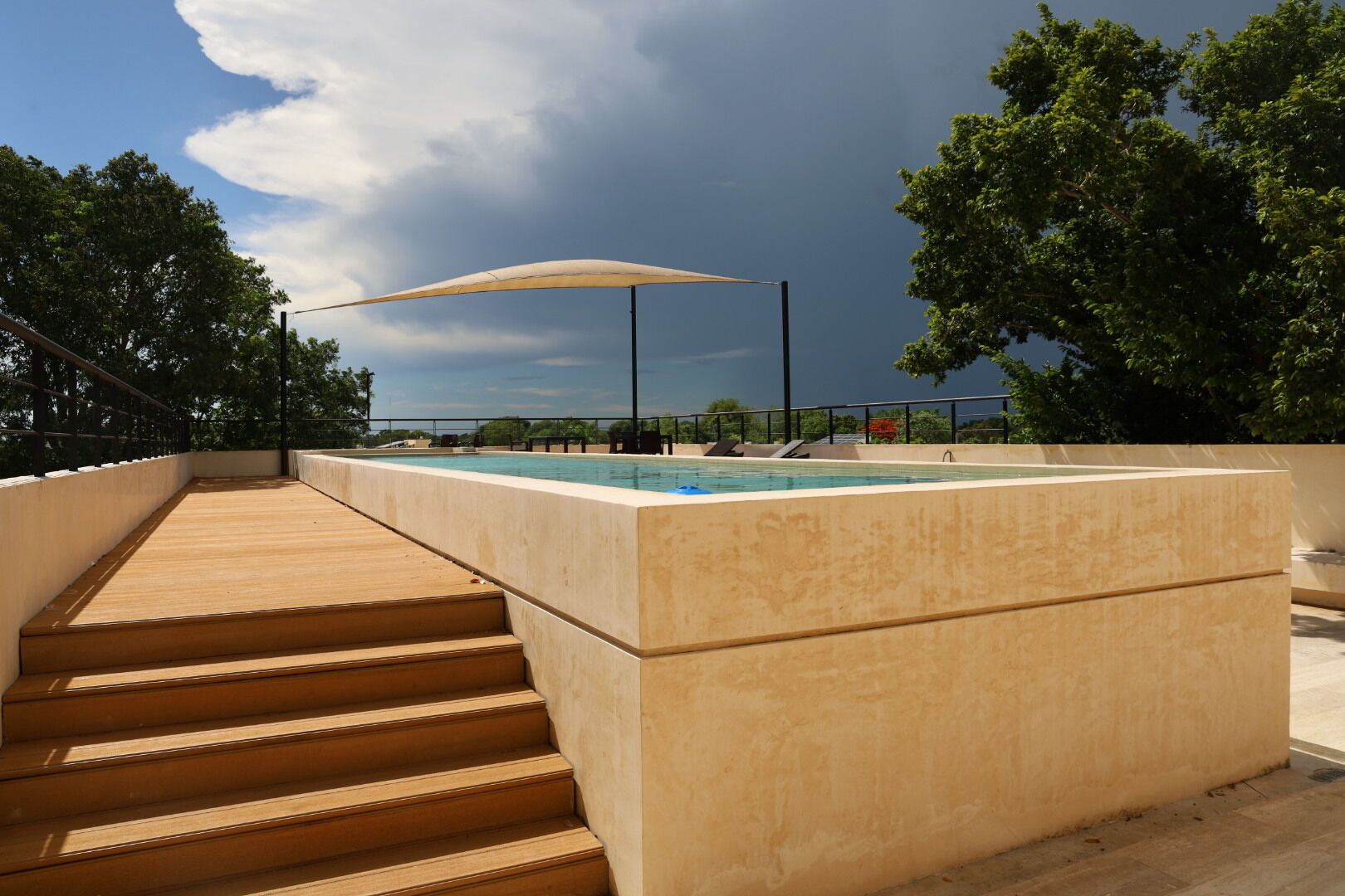 Une piscine sur le toit, dotée d’une terrasse en bois et d’un escalier menant à celle-ci, entourée d’arbres et surplombant un ciel dégagé.