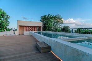 Uma área de piscina no terraço, com deck de madeira, piscina de concreto e um edifício moderno com parede de tijolos.