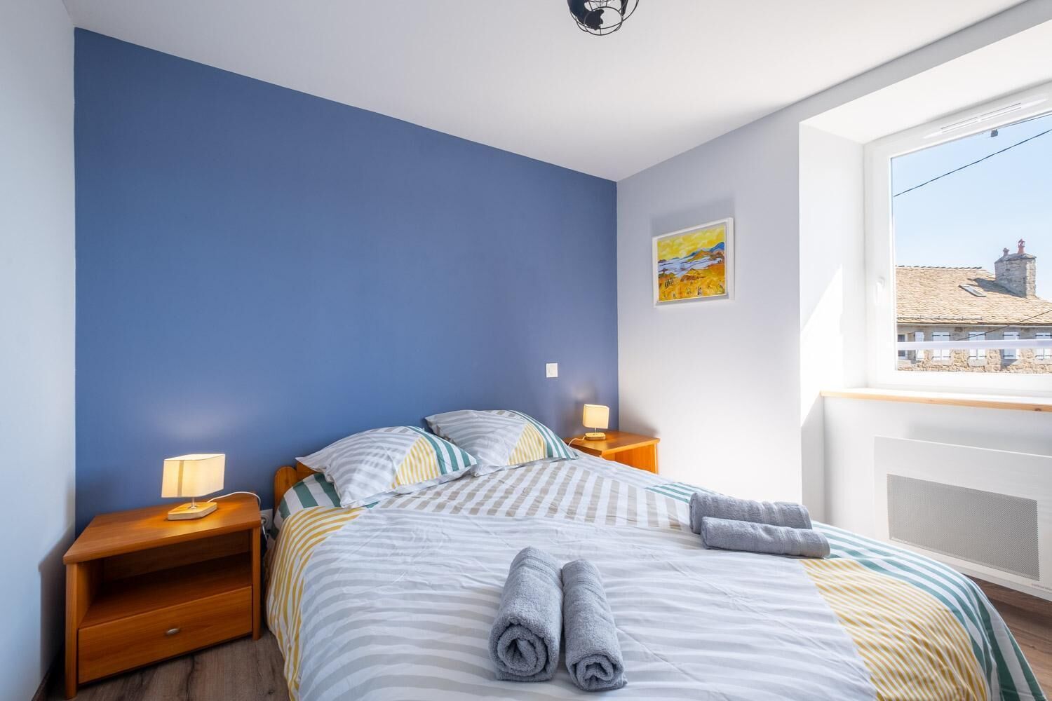 Une chambre à coucher avec un lit, deux tables de chevet, une fenêtre donnant sur un beau paysage et un tableau accroché au mur.