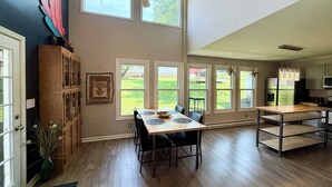 A spacious kitchen with large windows, a dining area with a wooden table, and a ceiling fan.
