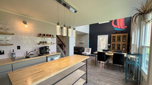 A modern kitchen with a wooden island, a dining area with a black sofa, and a large window with a view.