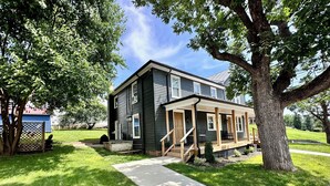 A two-story house with a covered porch, a front yard, and a tree.