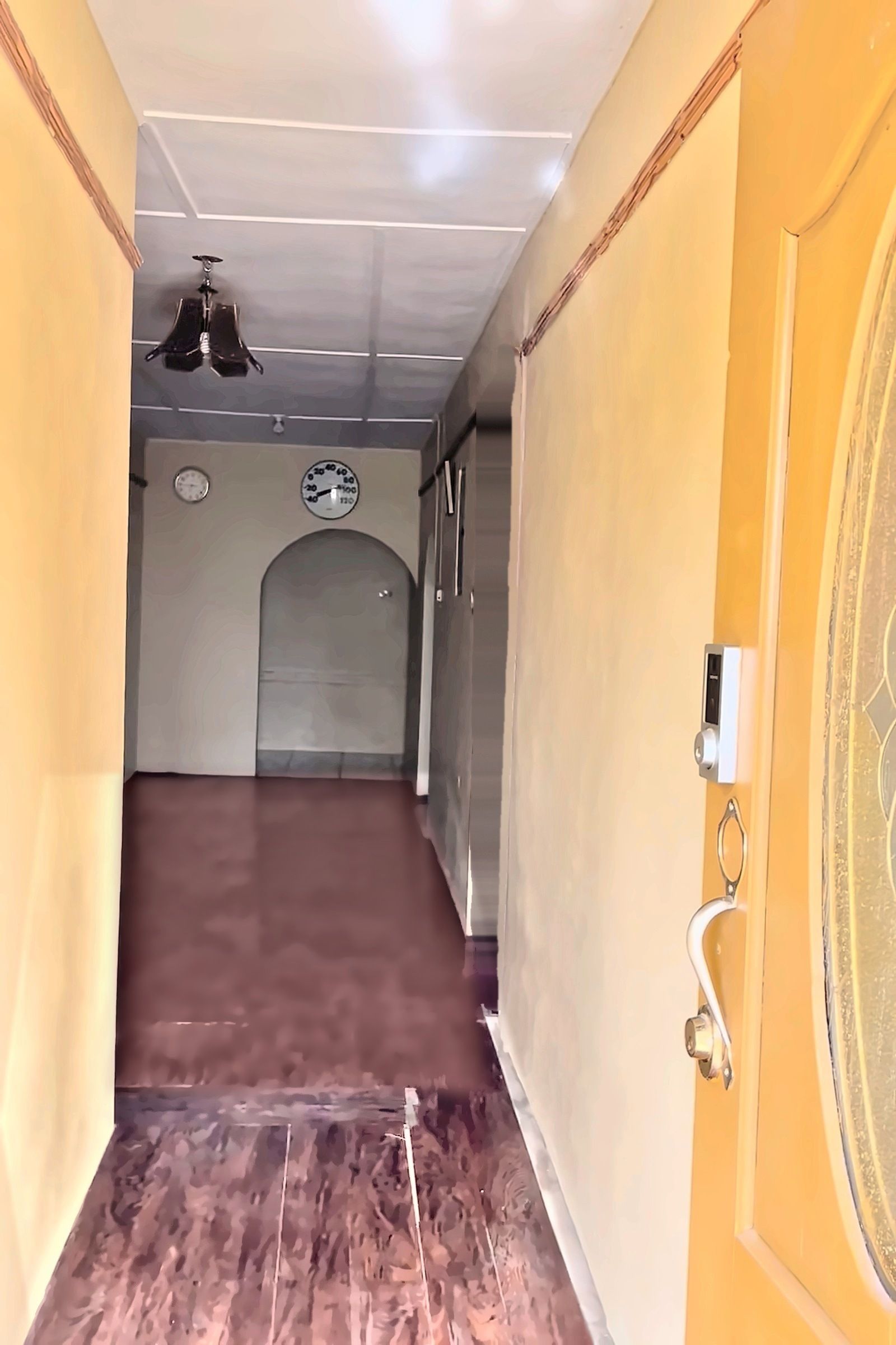 A hallway with a wooden door on the right, a clock on the wall, and a ceiling light fixture.