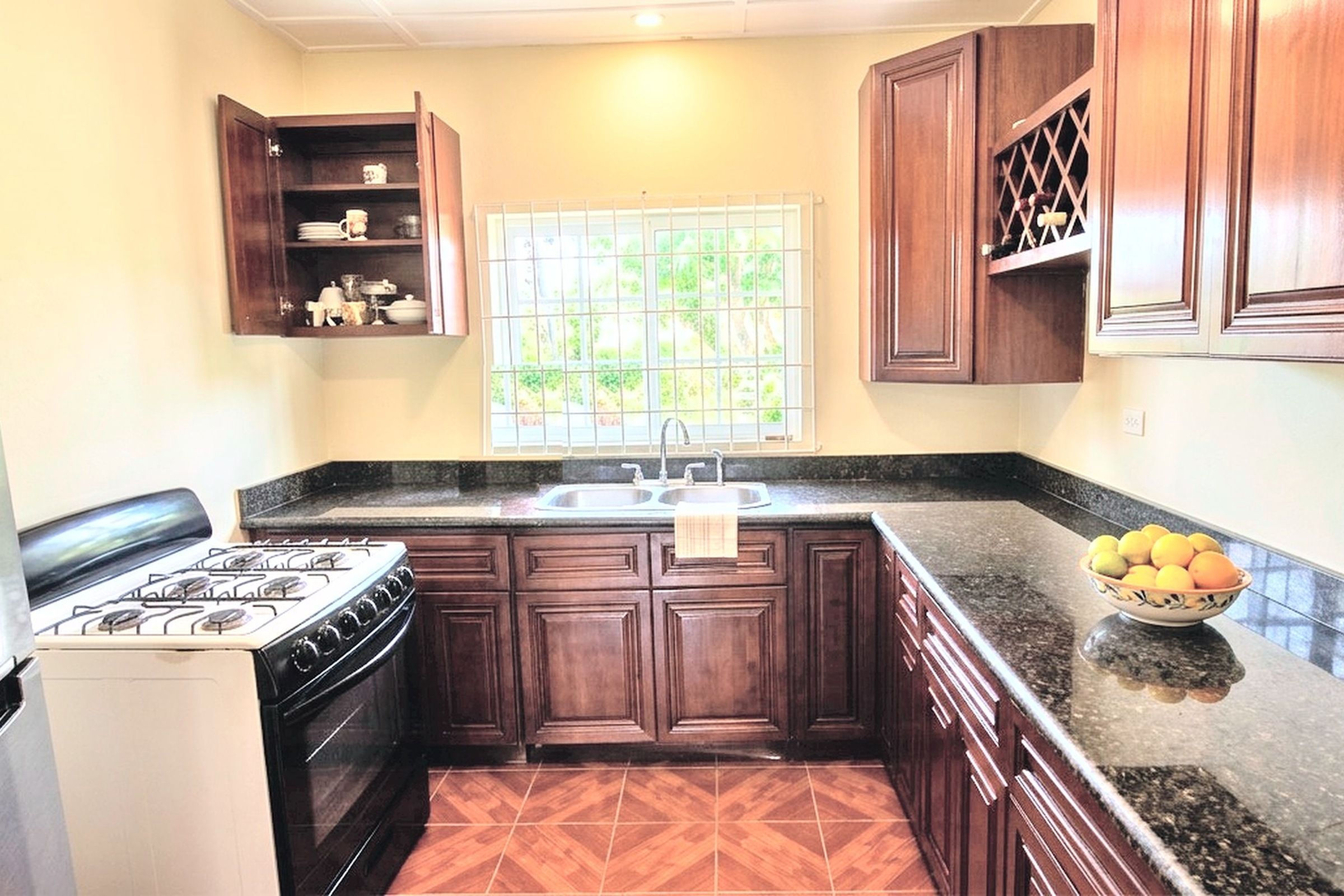 A kitchen with dark wooden cabinets, a gas stove, a sink, and a window with a view of greenery.