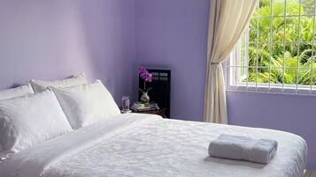 A bedroom with a bed, a nightstand, a window with curtains, and a view of greenery outside.